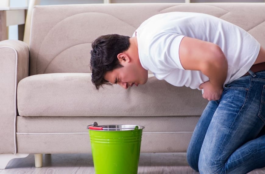 Homme penché sur un seau prêt à vomir