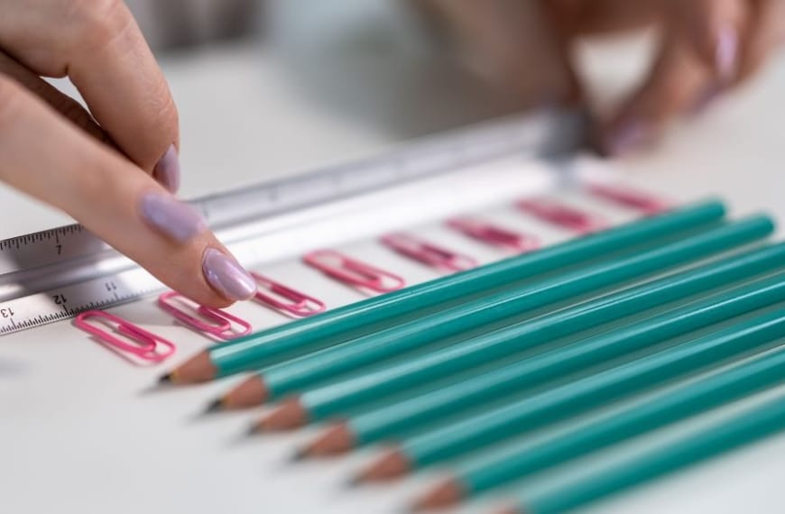 Pencils and paper clips laying in neat lines with a ruler fingers organising it