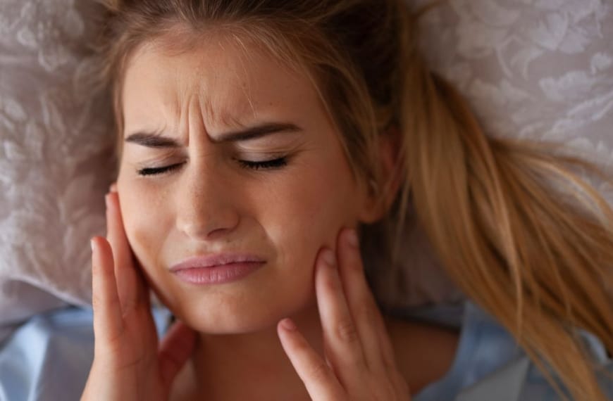 Woman holding her cheeks in pain after teeth grinding