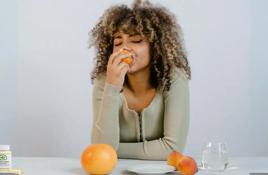 Vrouw geniet van een perzik aan een eettafel
