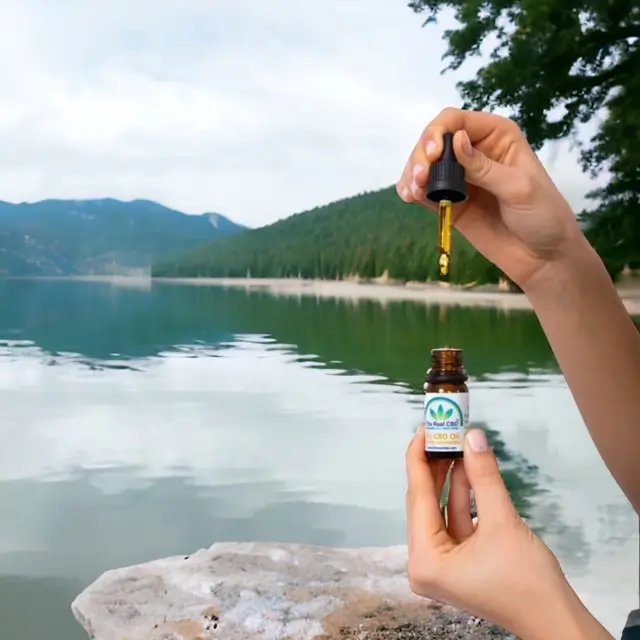 Hände mit geöffneter CBD-Tinkturflasche vor einem See - The Real CBD Brand