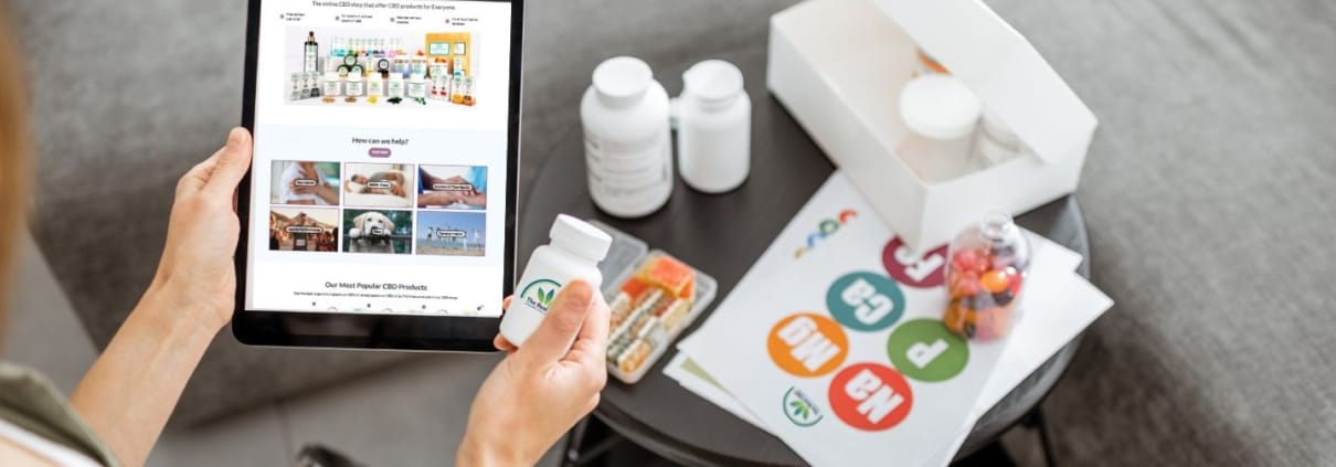 Man met een tablet met The Real CBD website erop en een potje The Real CBD tabletten