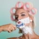 Woman with pin curlers shaving her beard