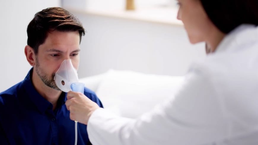 Homme respirant dans un masque à oxygène tenu par un médecin