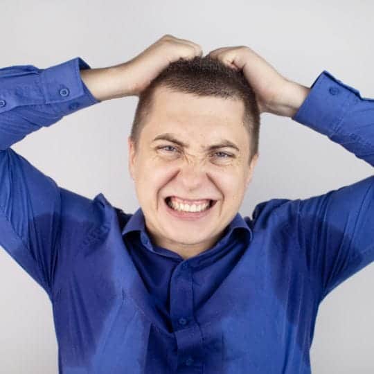 Persoon met overmatig zweten die zijn armen optilt en gefrustreerd kijkt