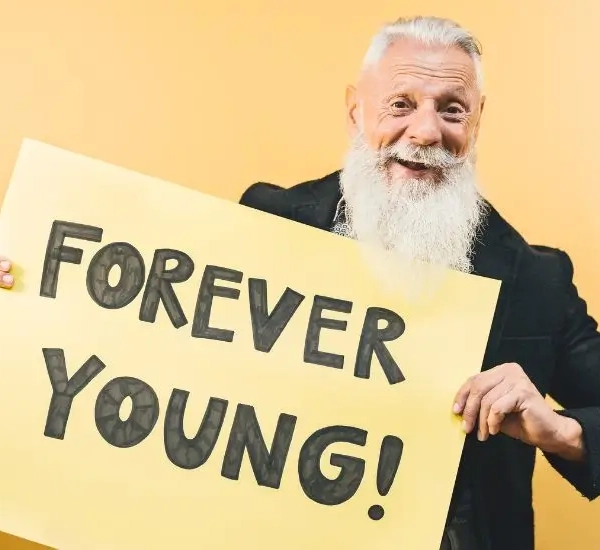 Older man looking happy holding a sign saying FOREVER YOUNG