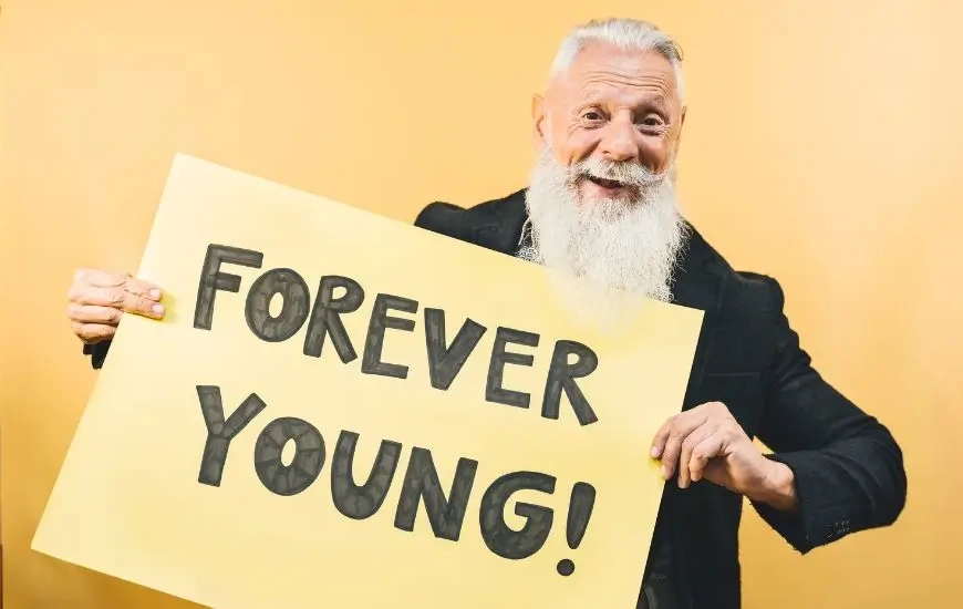 Older man looking happy holding a sign saying FOREVER YOUNG