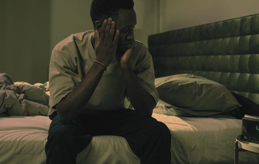 Man sitting on the edge of his bed at nighttime unable to sleep