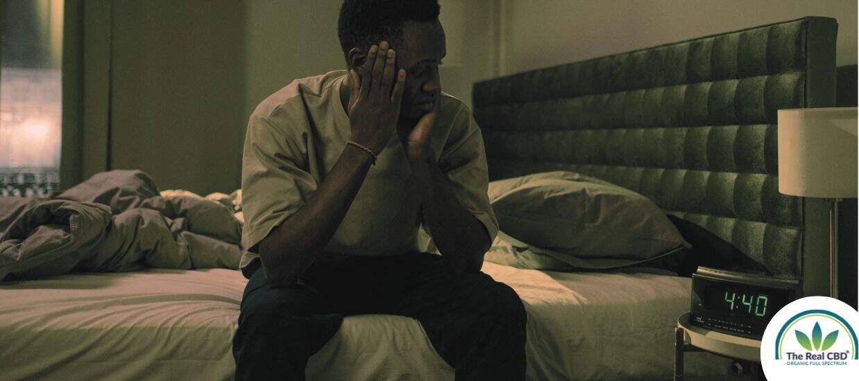 Man sitting on the edge of his bed at nighttime unable to sleep
