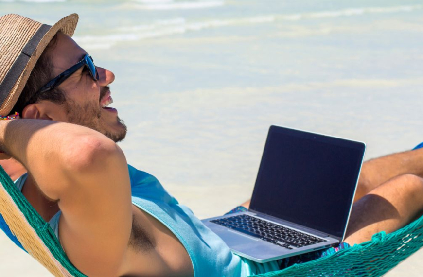 Happy man in a hammock on the beach working on his laptop