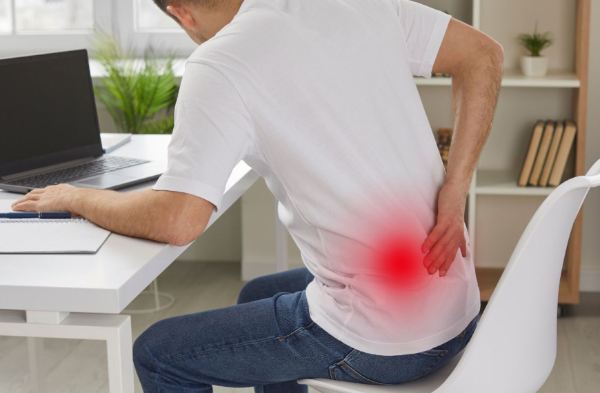 Man sitting at his desk holding his lower back in pain