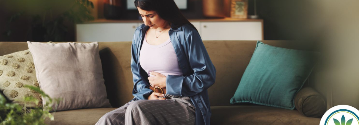 Woman sitting on a sofa holding her stomach in pain