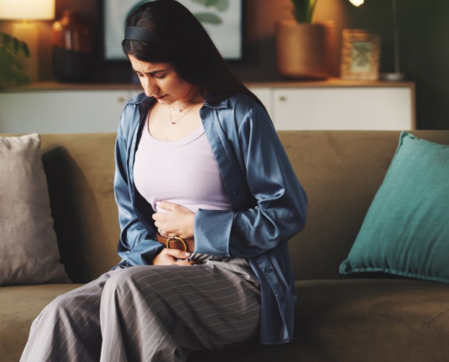 Woman sitting on a sofa holding her stomach in pain