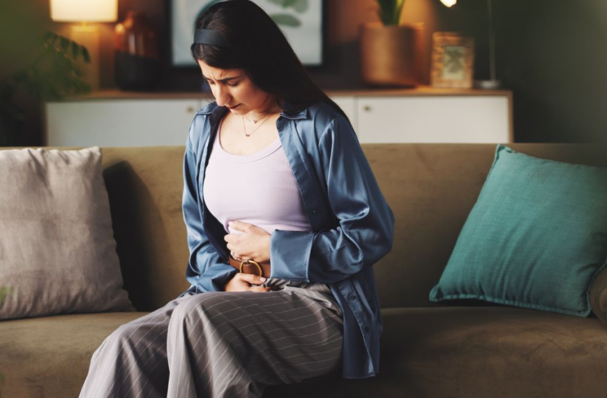 Woman sitting on a sofa holding her stomach in pain