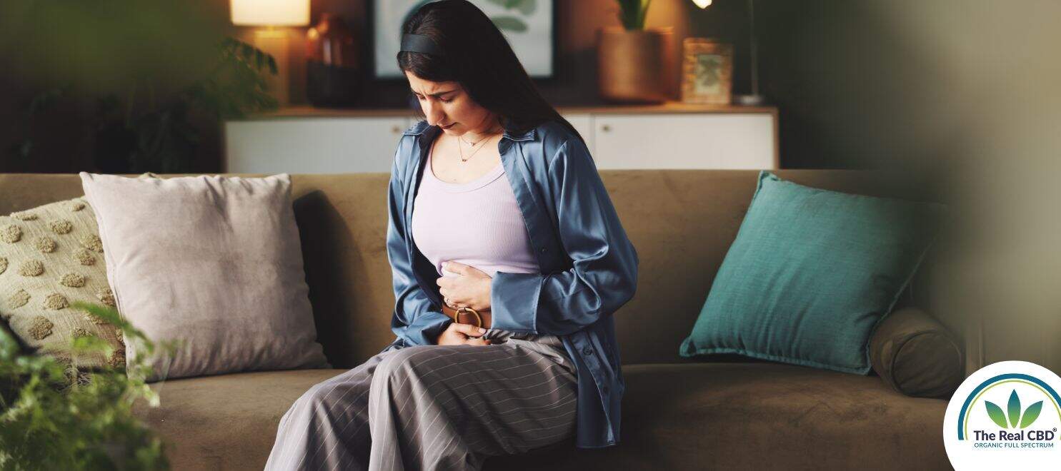 Woman sitting on a sofa holding her stomach in pain