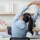 Woman sitting by a desk stretching her arms over her head