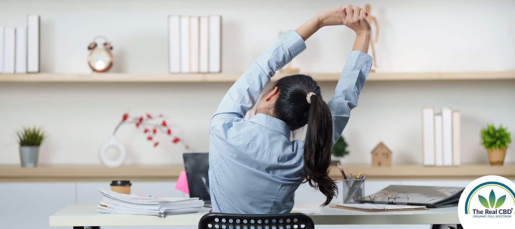 Woman sitting by a desk stretching her arms over her head